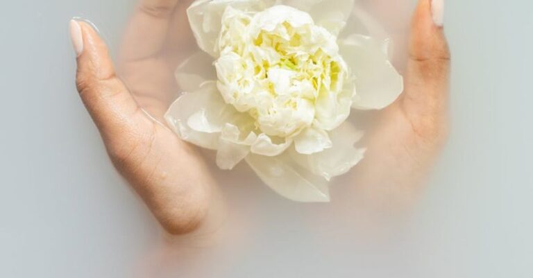 Natural Skincare - Unrecognizable female with soft manicured hands holding white flower with delicate petals in hands during spa procedures