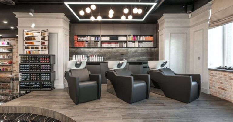 Wellness Trends - Black leather backwash chairs with sinks under glowing lamps placed in modern spacious beauty salon with cosmetology products and window